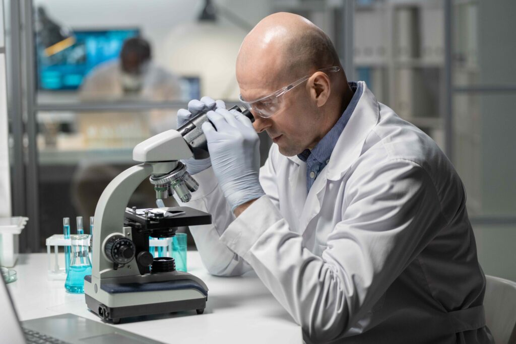man in research lab looking through microscope